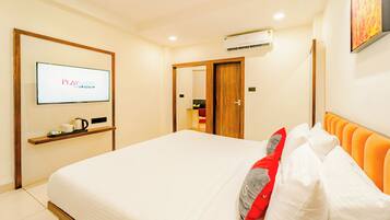 A hotel room with a bed, a TV mounted on the wall, a shelf with a coffee pot, and an air conditioning unit.