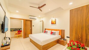 A modern hotel room with a large bed, a wooden headboard, a bedside table with a phone, and a wall-mounted TV. - Playsales By Playotel (Indore)