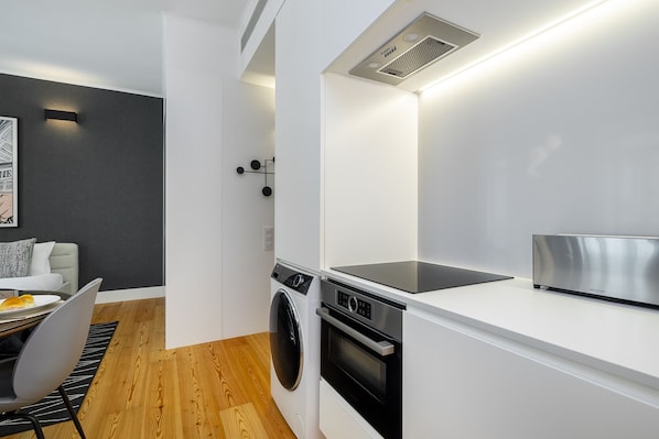 A compact kitchen with a washing machine, oven, and a built-in microwave.