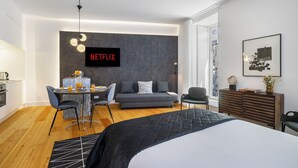 A modern hotel room with a bed, a sofa, a dining area, and a wall-mounted TV displaying 'NETFLIX'. - Exclusive City Hideaway (Lisbon)