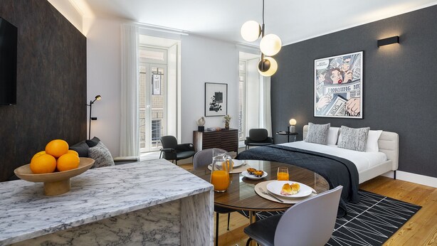 A modern hotel room with a bed, a dining area with a marble table, and a breakfast setup. - Exclusive City Hideaway (Lisbon)