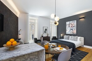 A modern hotel room with a bed, a dining area with a marble table, and a breakfast setup.