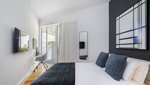 A modern bedroom with a large bed, a desk with a chair, a television, and a large window with curtains. - Exclusive City Hideaway (Lisbon)