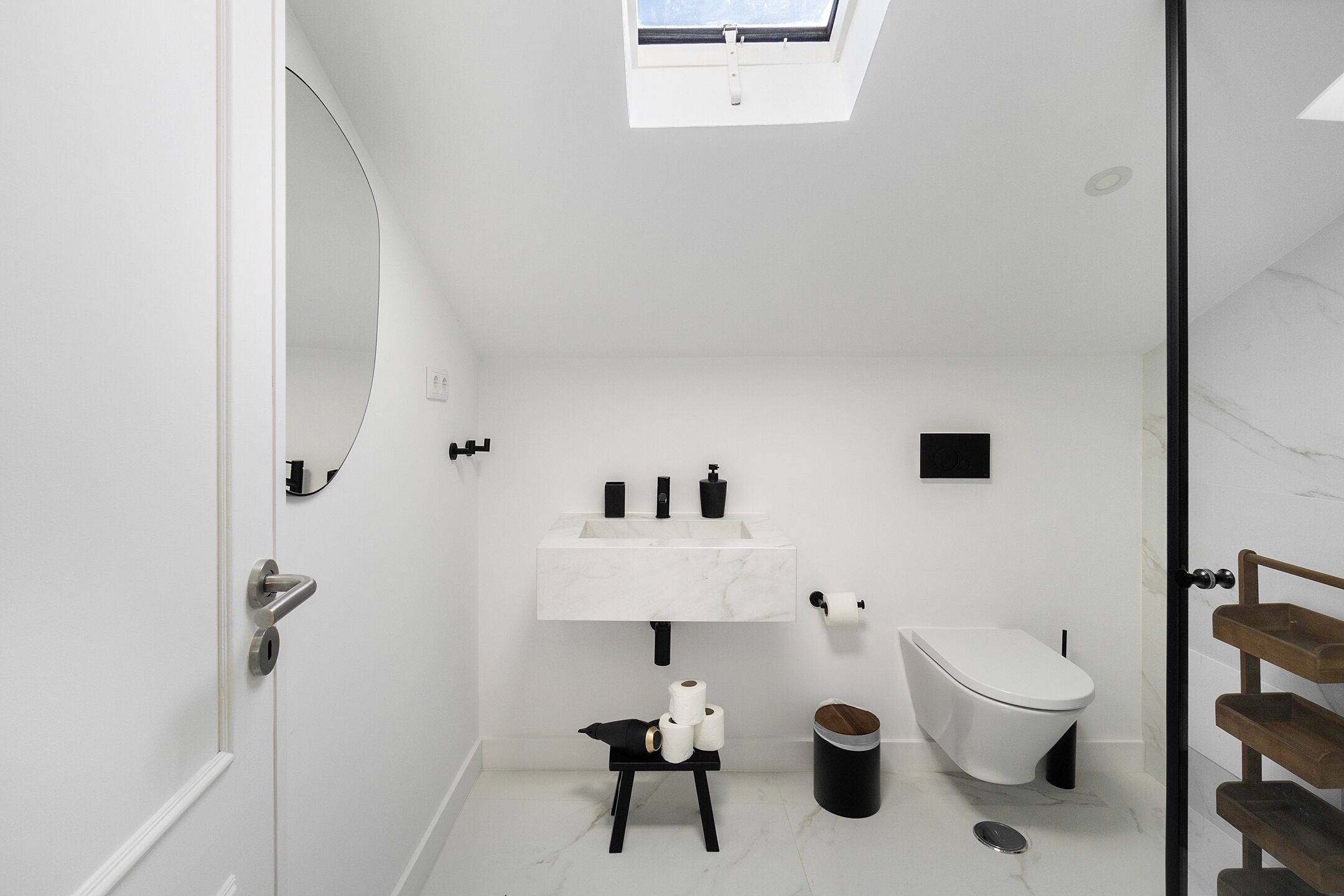 A modern bathroom with a skylight, a white sink, a toilet, and a small wooden stool.