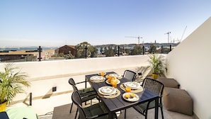 Uma área de refeições no terraço com uma mesa posta para quatro pessoas, com vista para um horizonte urbano com guindastes.