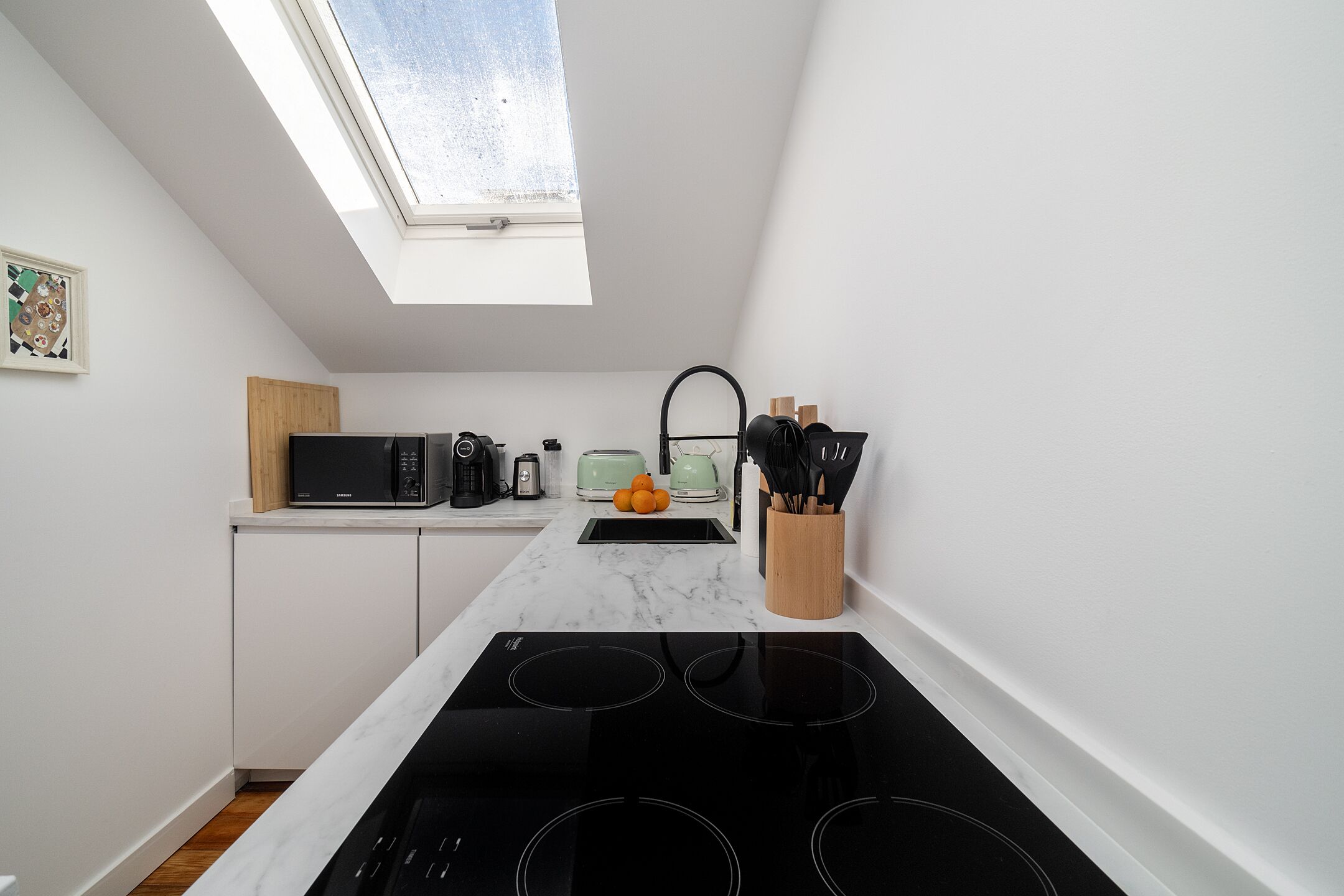 A modern kitchen with a skylight, white cabinets, a black stove, and a microwave.