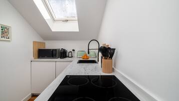 A modern kitchen with a skylight, white cabinets, a black stove, and a microwave.