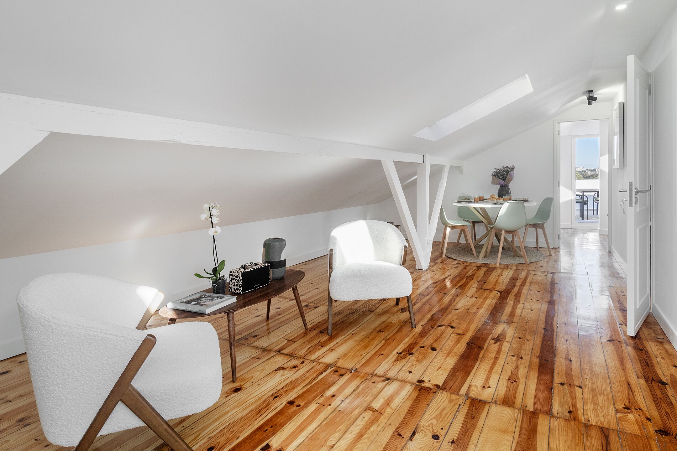 A modern loft with wooden flooring, white walls, and a dining area with a table and chairs.