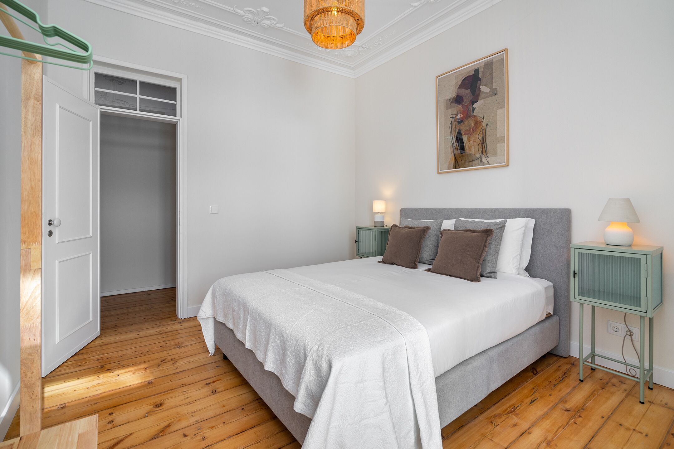 A bedroom with a large bed, a wardrobe, a bedside table with a lamp, and a painting on the wall.