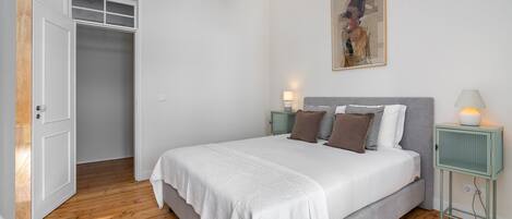 A bedroom with a large bed, a wardrobe, a bedside table with a lamp, and a painting on the wall.