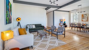 Uma sala de estar ampla com sofá, cadeiras, mesa de centro e um espaço de jantar com mesa e cadeiras.