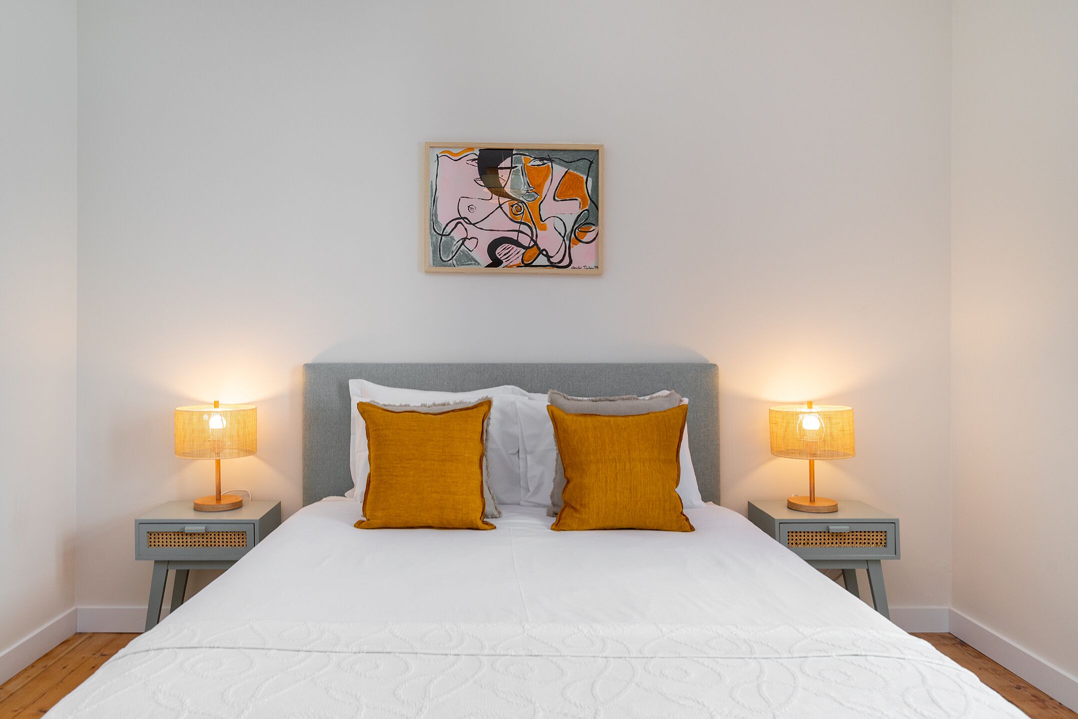 A bedroom with a large bed, two bedside lamps, a headboard, and a wall-mounted abstract painting.
