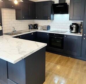 A modern kitchen with dark cabinets, a marble countertop, and a built-in oven. - Modern Gable end 2bed Cottage in the Ribble Valley (Burnley)