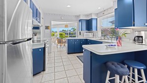 A modern kitchen with blue cabinets, a stainless steel refrigerator, and a central island with stools. - Tropical Canal Home–Pool, Sun & Water Access: Paradise Cottage in LBK by RVA (Longboat Key)