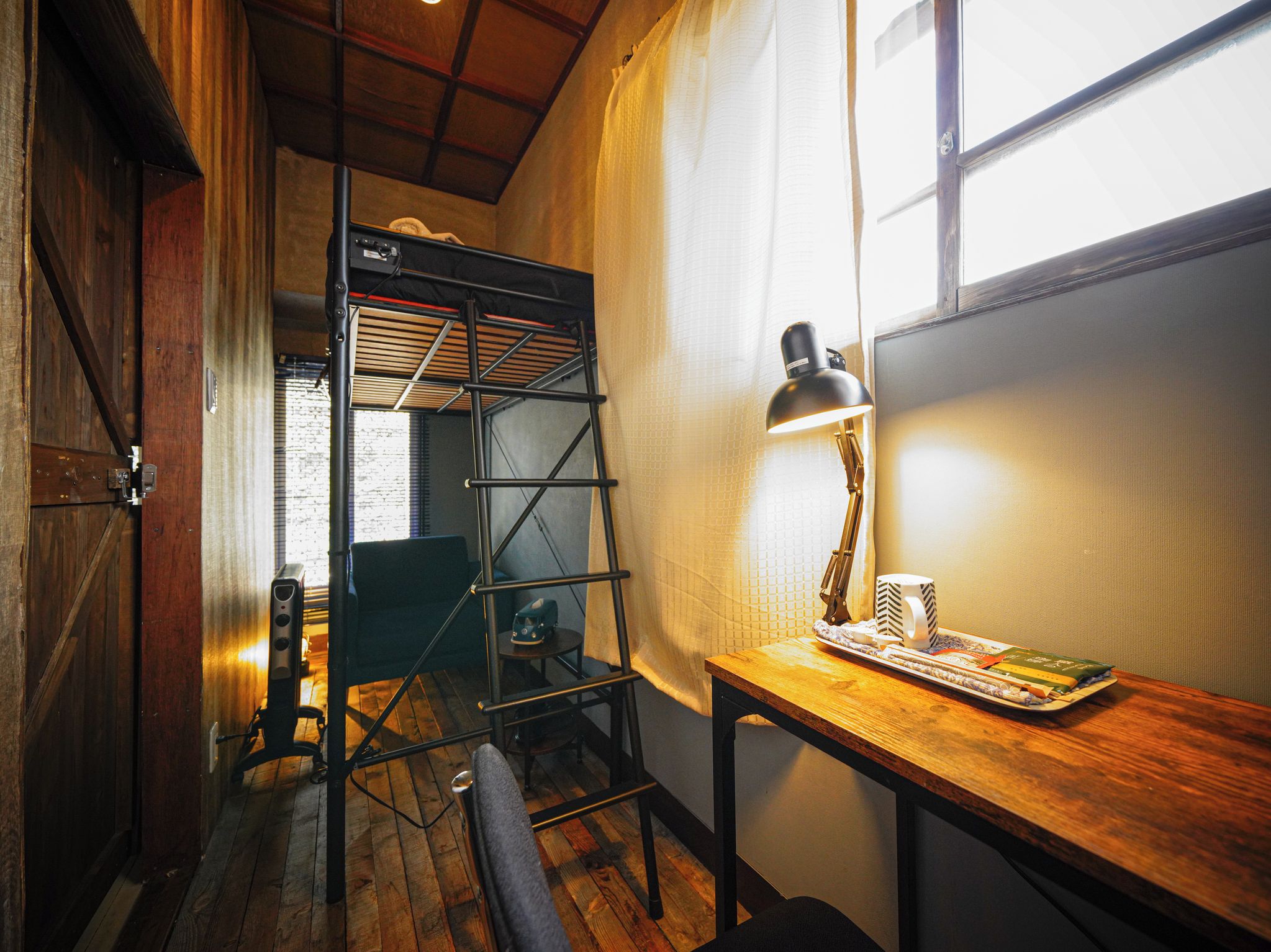Een kamer met houten vloer, een bureau met lamp, een stoel en een raam met gordijnen.