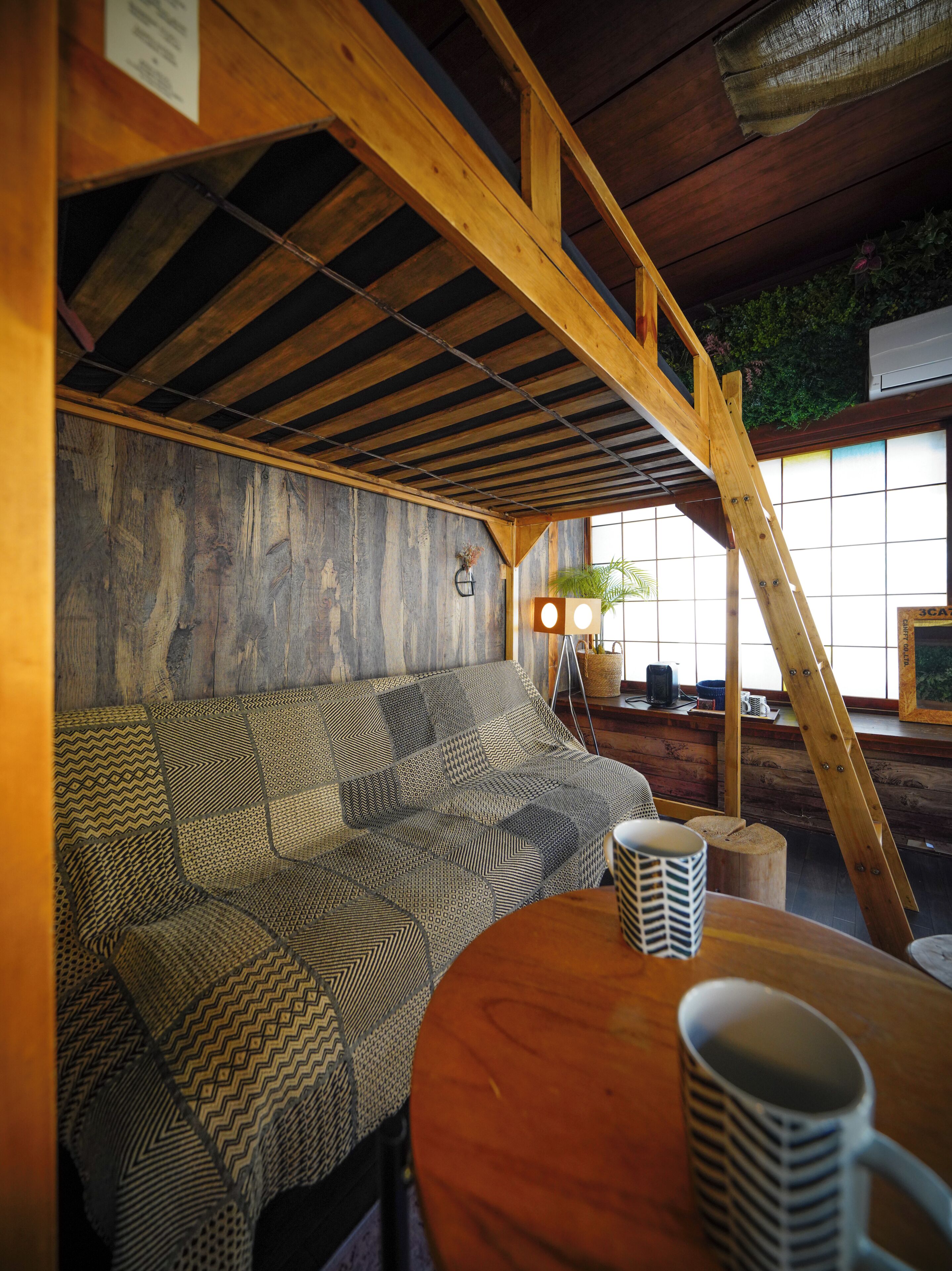 A wooden interior with a sofa, a table with mugs, and a ladder.