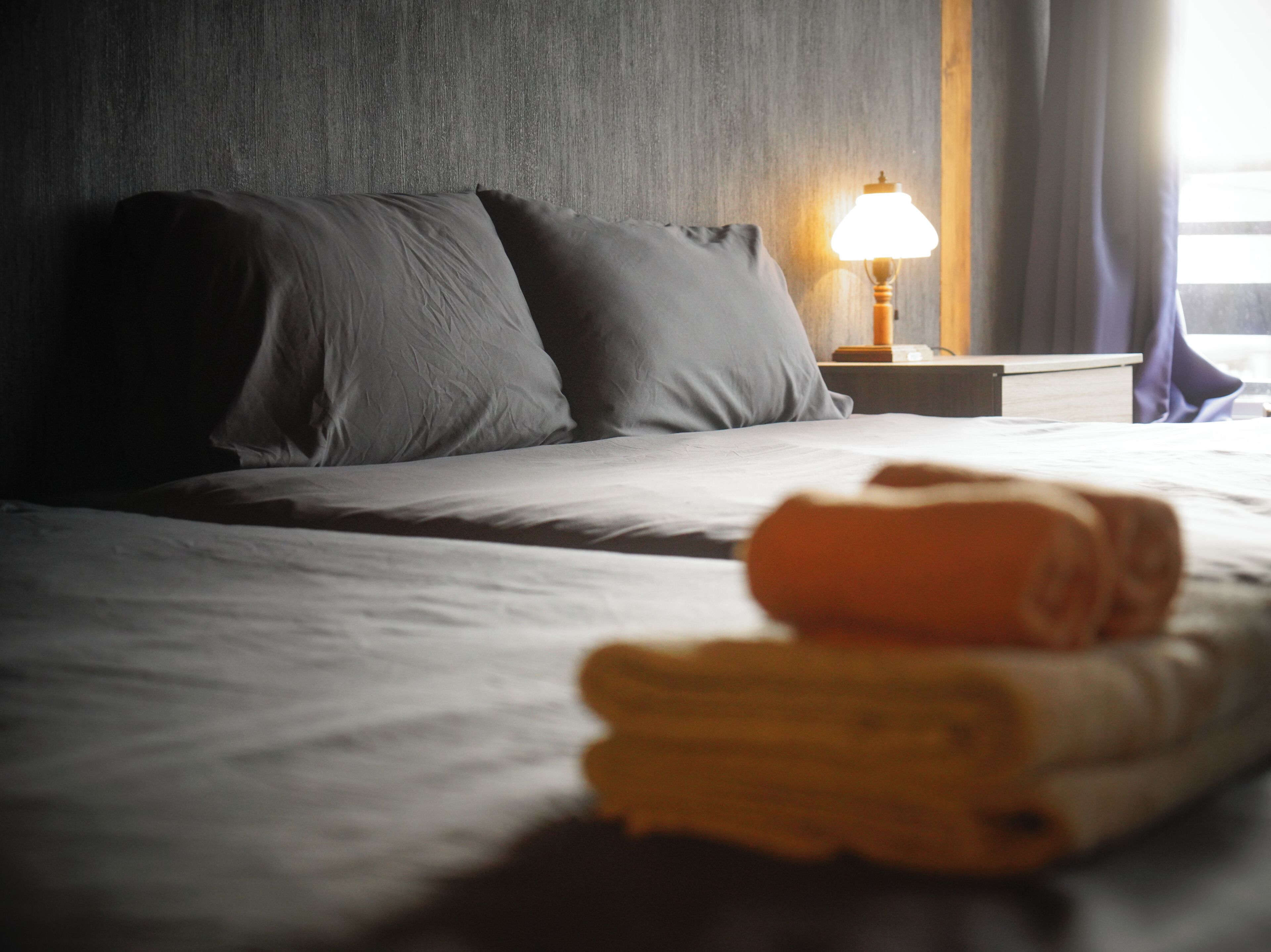 A neatly made bed with pillows, a lamp on the nightstand, and a rolled towel on the bed.