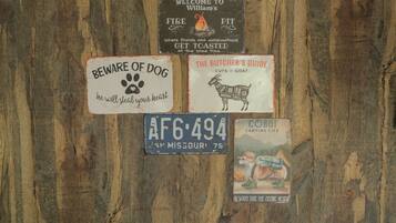 A wooden wall with various signs including a 'Beware of Dog' sign, a welcome sign, a butcher's guide, a license plate, and a camping life sign.