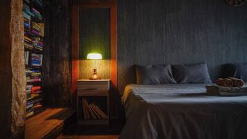 Quarto com estante de madeira, mesa de cabeceira com abajur, cama com almofadas e relógio de parede.