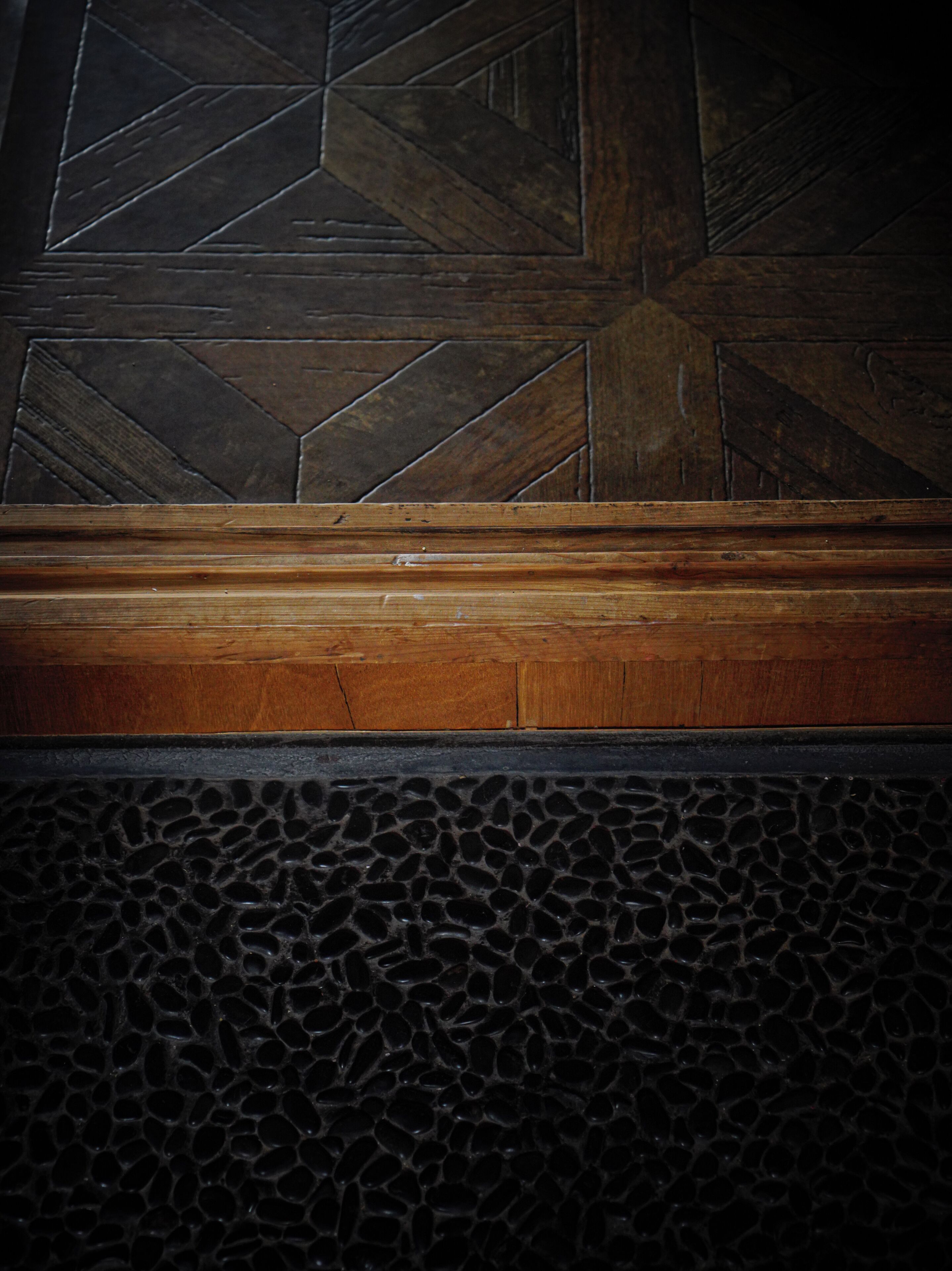 A wooden bench with a geometric patterned wall behind it.