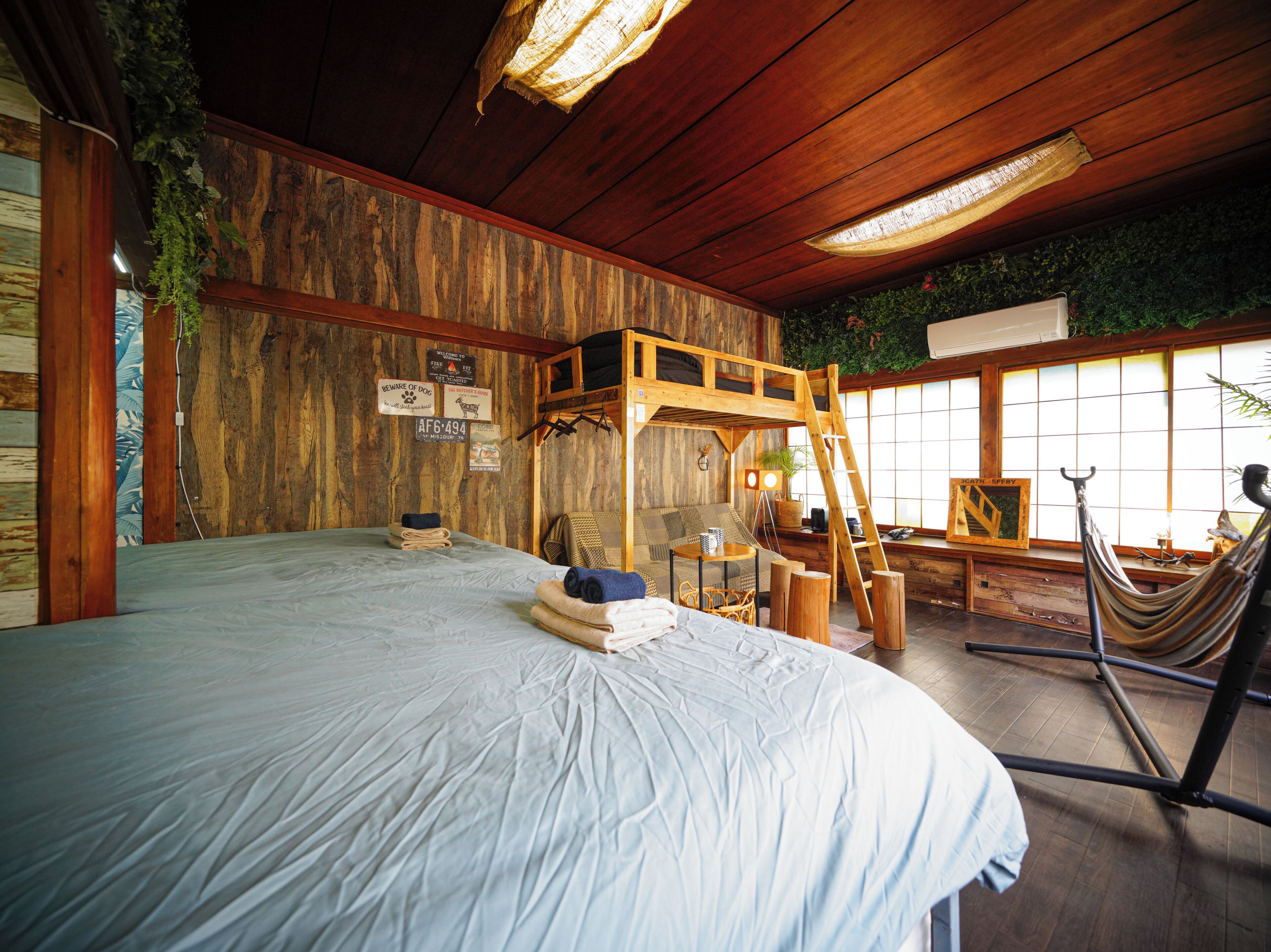 A rustic room with a bed, a hammock, a ladder, and a wooden ceiling.