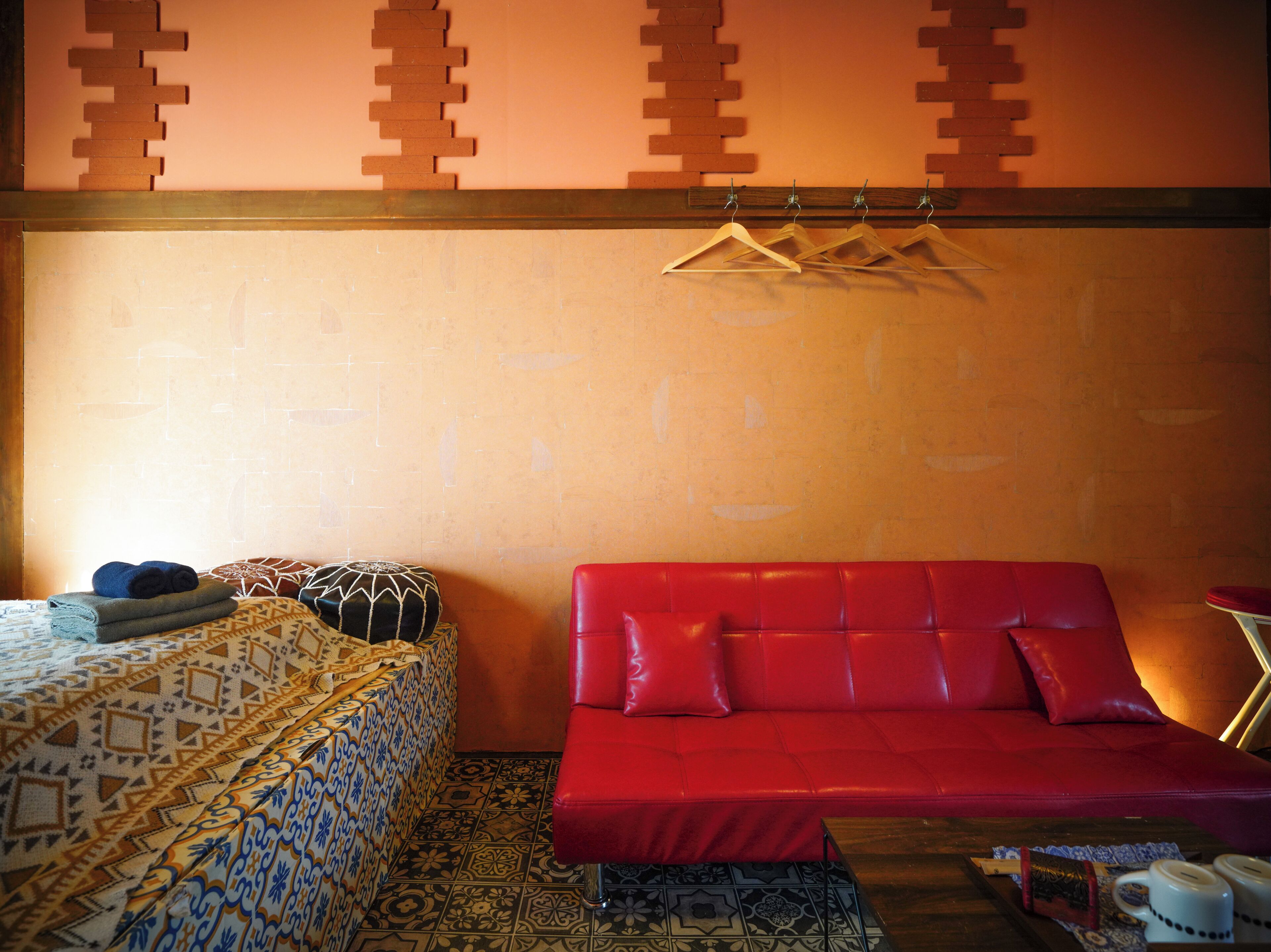 A room with a patterned bed, a red sofa, a hanging clothes rack, and a small table with a cup and a book.