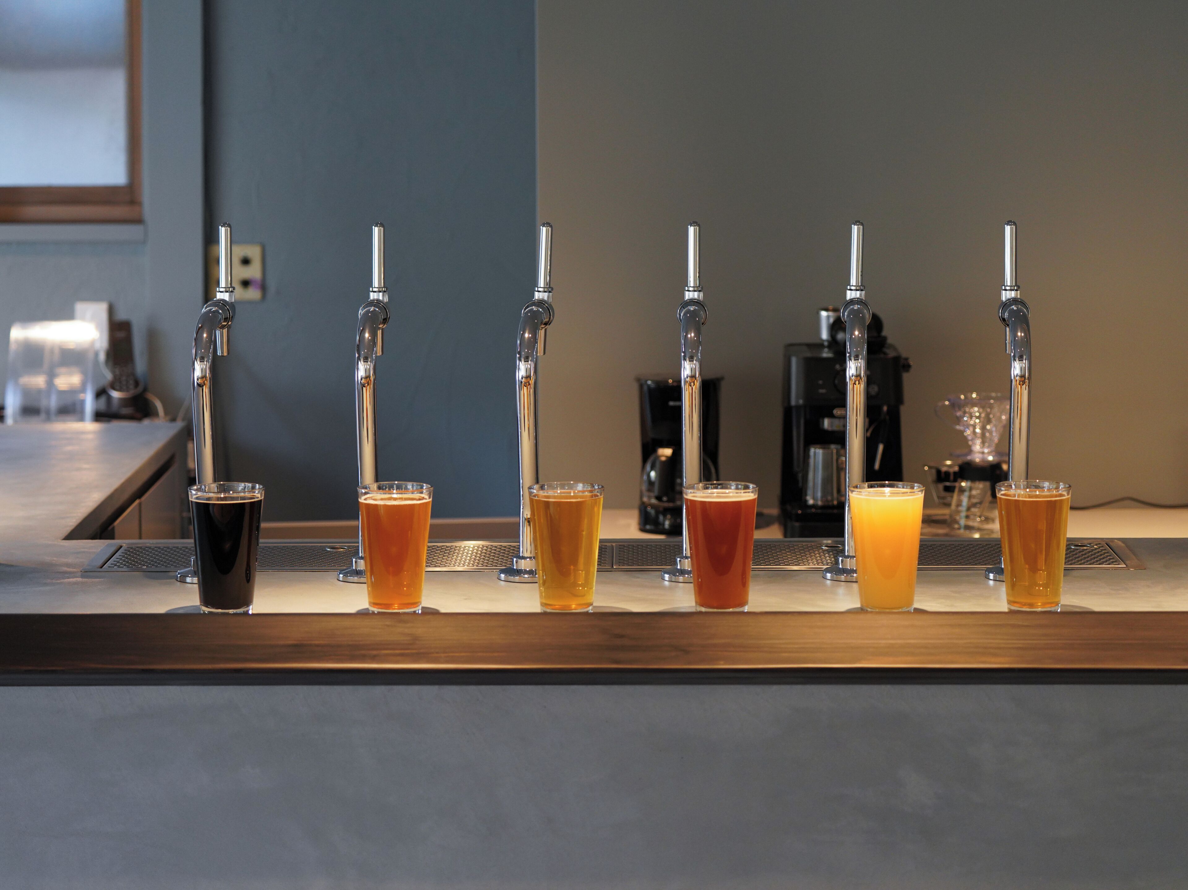 A bar with six taps dispensing different beverages, a coffee machine, and a counter.