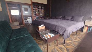 A bedroom with a bed, a green sofa, a wooden nightstand, and a bookshelf filled with books.