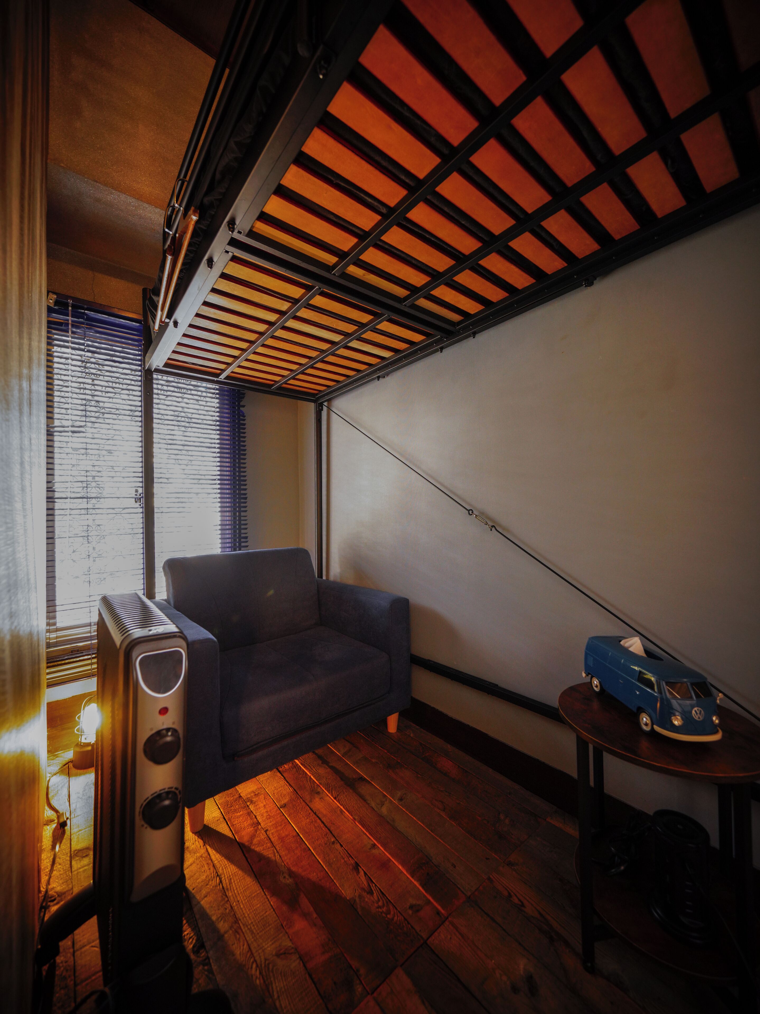 A room with a wooden floor, a sofa, a radiator, a small table with a toy car, and a window with blinds.