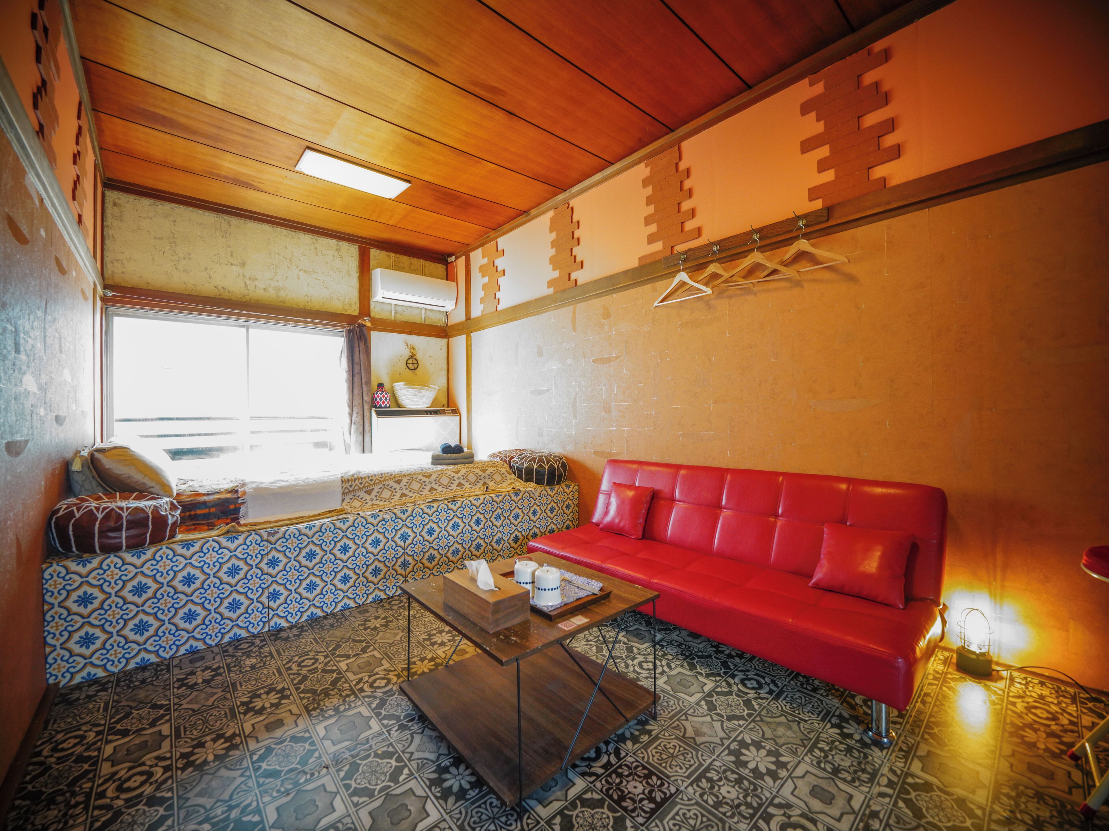 A room with a red sofa, patterned tiles, a wooden ceiling, and a window.