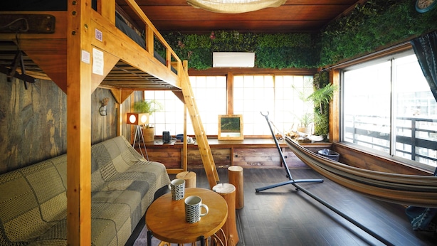Un interior de madera con una hamaca, un sofá, una mesa con tazas y vistas amplias a través de grandes ventanales.