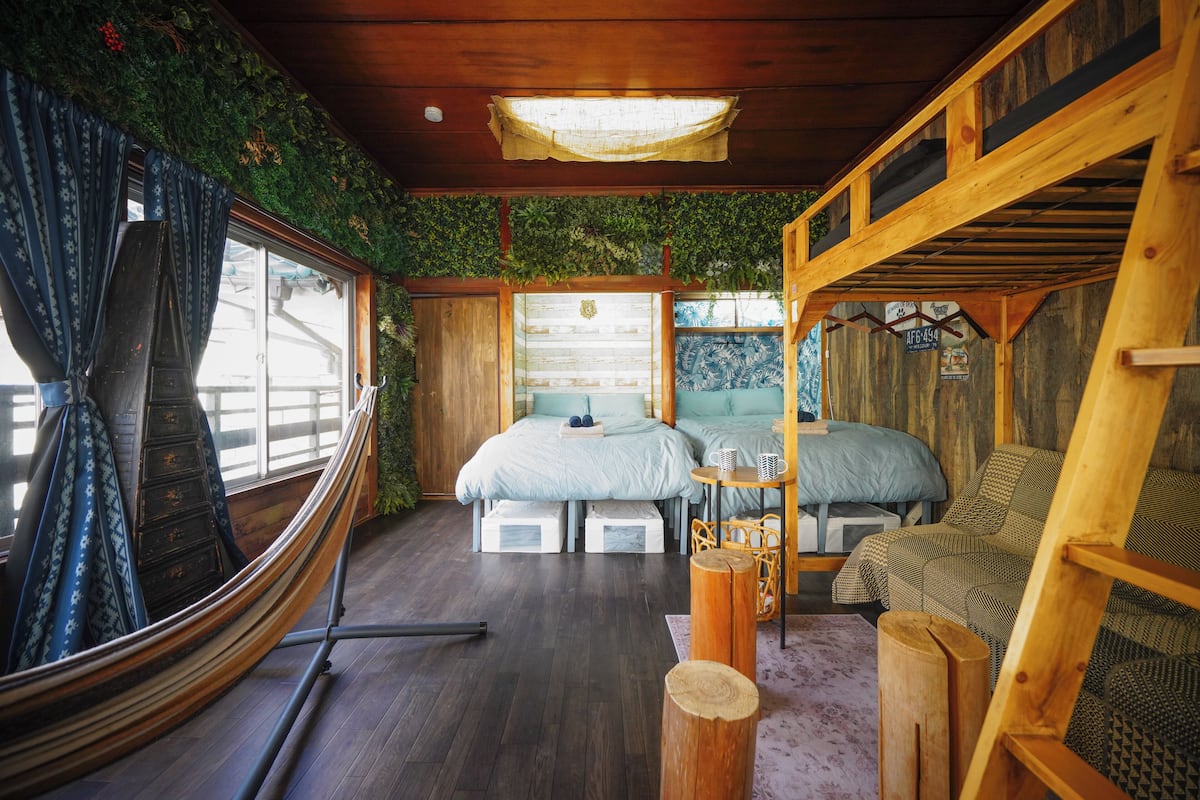Una cabaña con interior de madera, dos camas, una mesita y una hamaca.