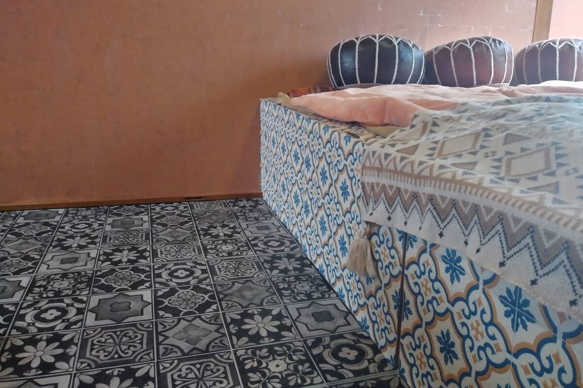 Una habitación con una colcha estampada, un papel tapiz decorado y un suelo de baldosas.