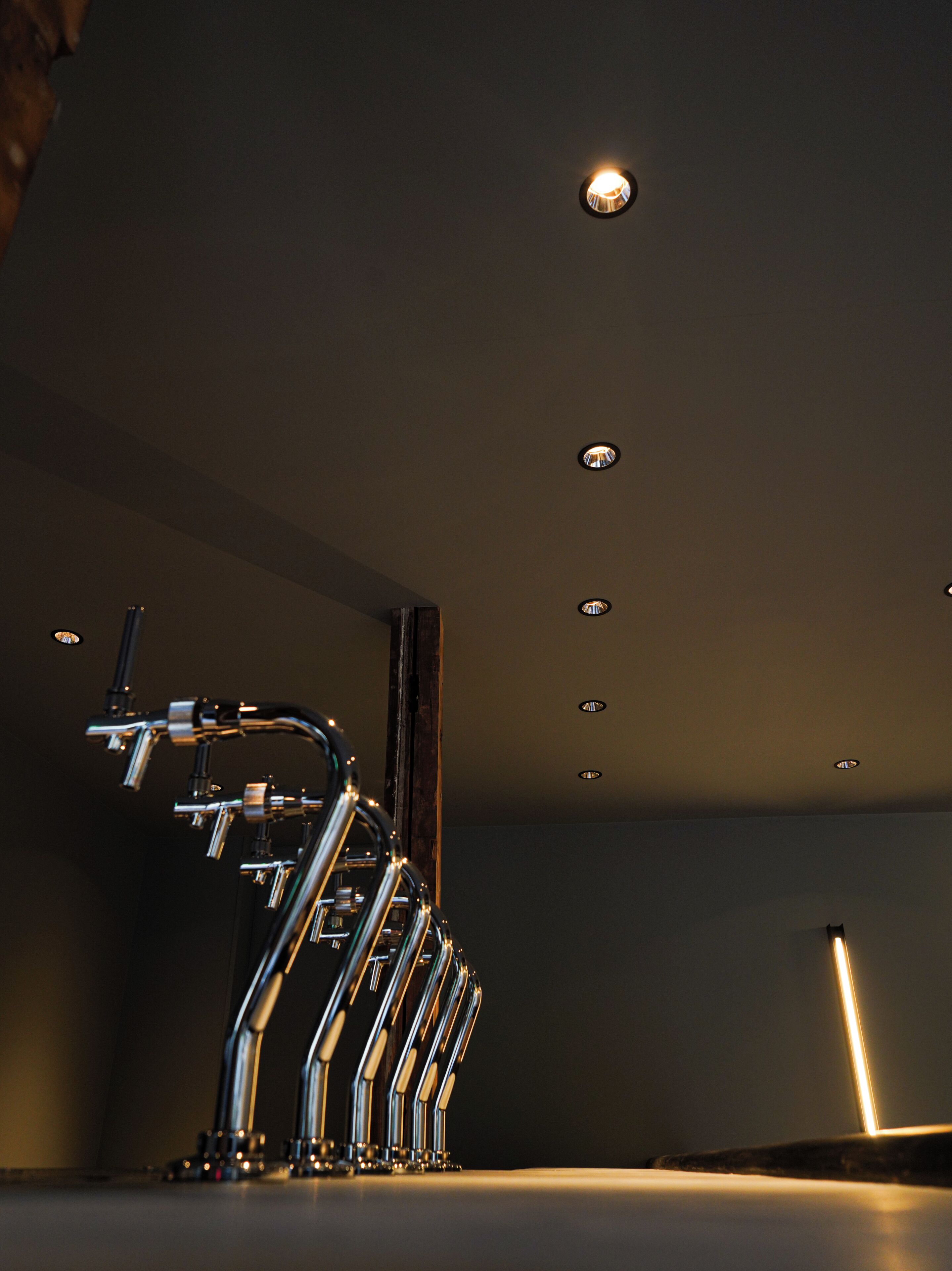 A modern bathroom with a unique faucet design, recessed ceiling lights, and a wooden column.