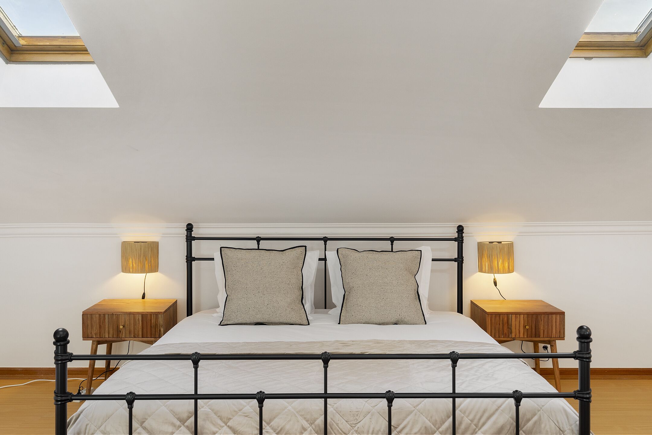 A bedroom with a bed, two bedside tables, and a skylight.