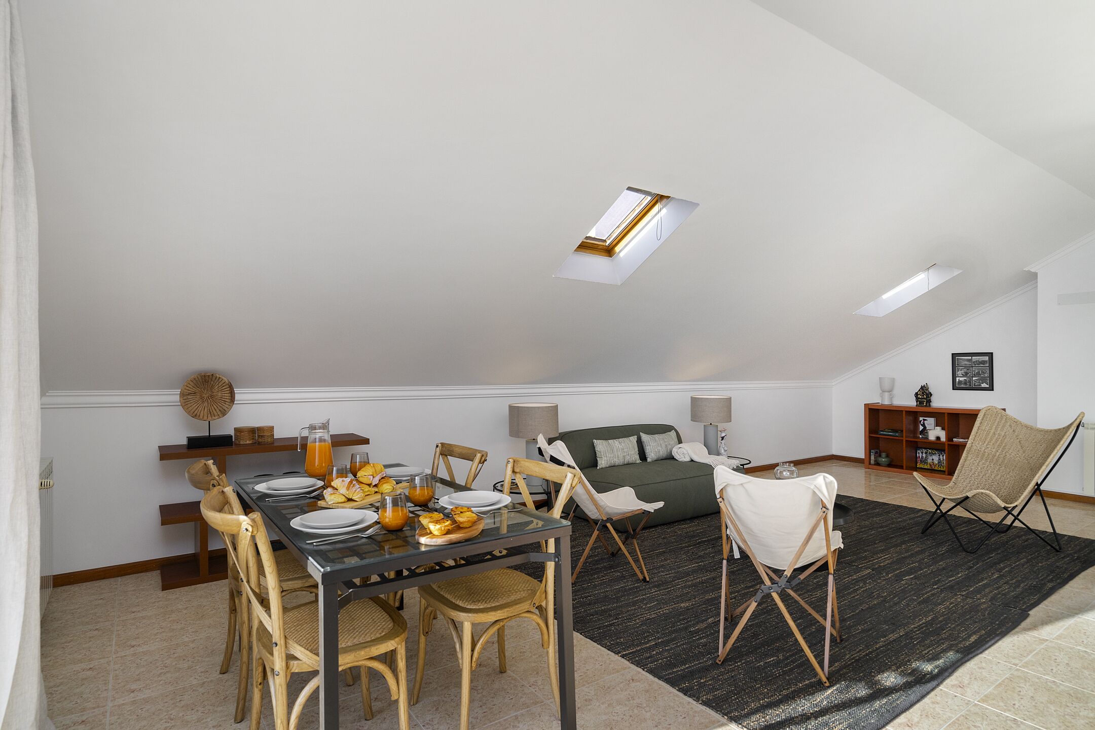 A dining area with a table set for breakfast, a sofa, and a bookshelf.