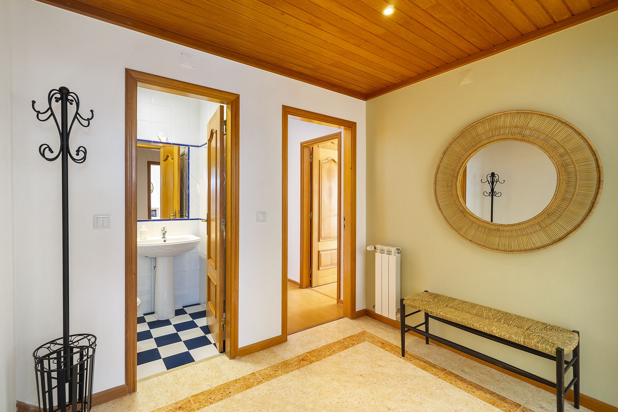 A hallway with a checkered floor, a bench, a round mirror, and a radiator.