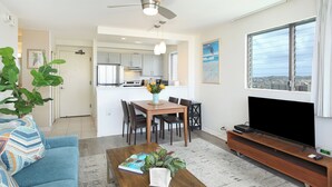 A modern living room with a sofa, coffee table, TV, and dining area. - Great Partial Ocean View! Full Kitchen, Free Parking, Pool! Heart of Waikiki! (Honolulu)
