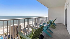 Un balcon avec vue sur la plage et l’océan. On y trouve des chaises vertes et une table.