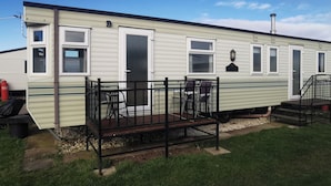 Une maison mobile dotée d’une terrasse, d’une porte, de fenêtres et d’une cheminée.