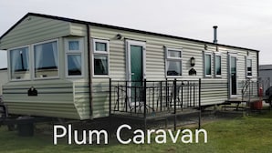 Une maison mobile dotée d’une véranda et d’une cheminée, portant l’inscription « Plum Caravan ».