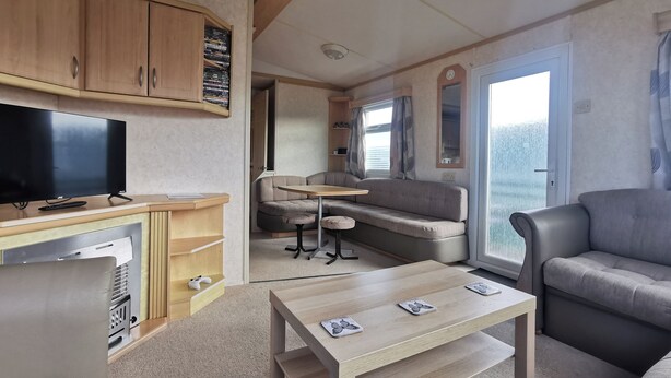 Un espace de vie compact comprenant un téléviseur, des meubles en bois, un canapé, une table et une fenêtre avec des rideaux.