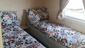 Une petite chambre avec un lit simple, dotée de draps à motifs floraux et d’une fenêtre avec des rideaux.