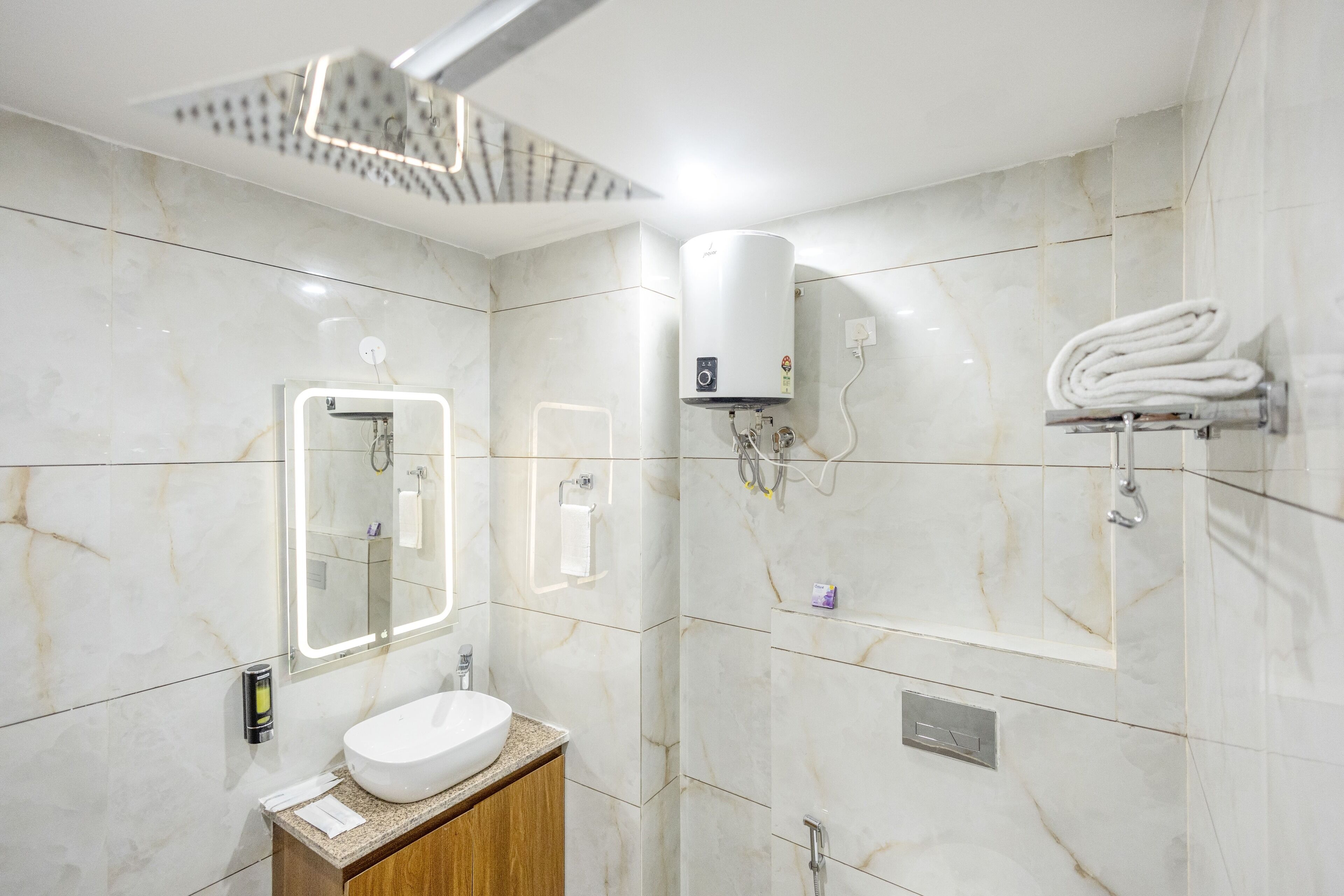 A modern bathroom with a marble wall, a sink, a mirror, a towel rack, and a shower head.