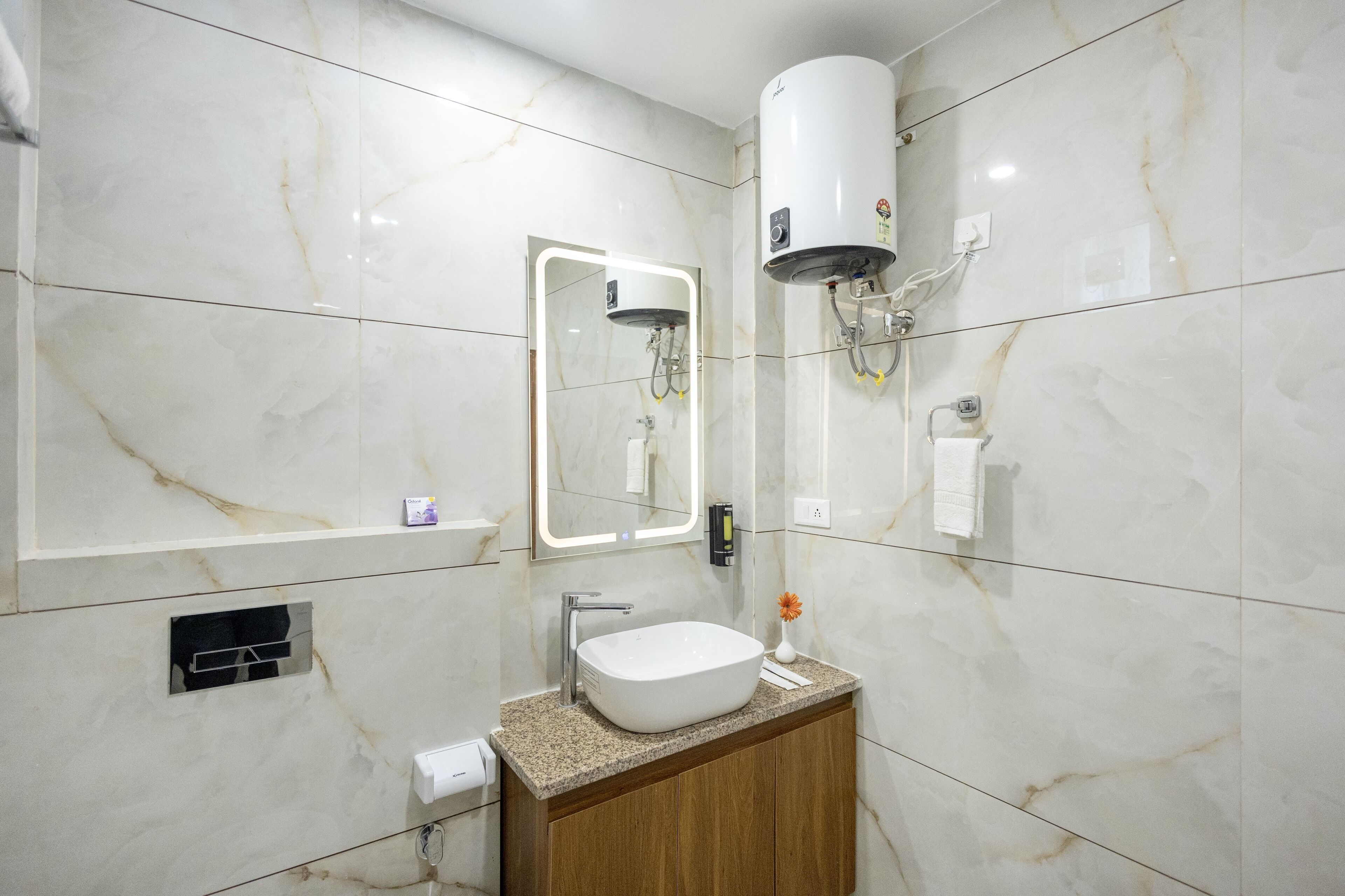 Een moderne badkamer met een marmeren wand, een inbouwwastafel, een spiegel, een handdoekhouder en een wandradiator.