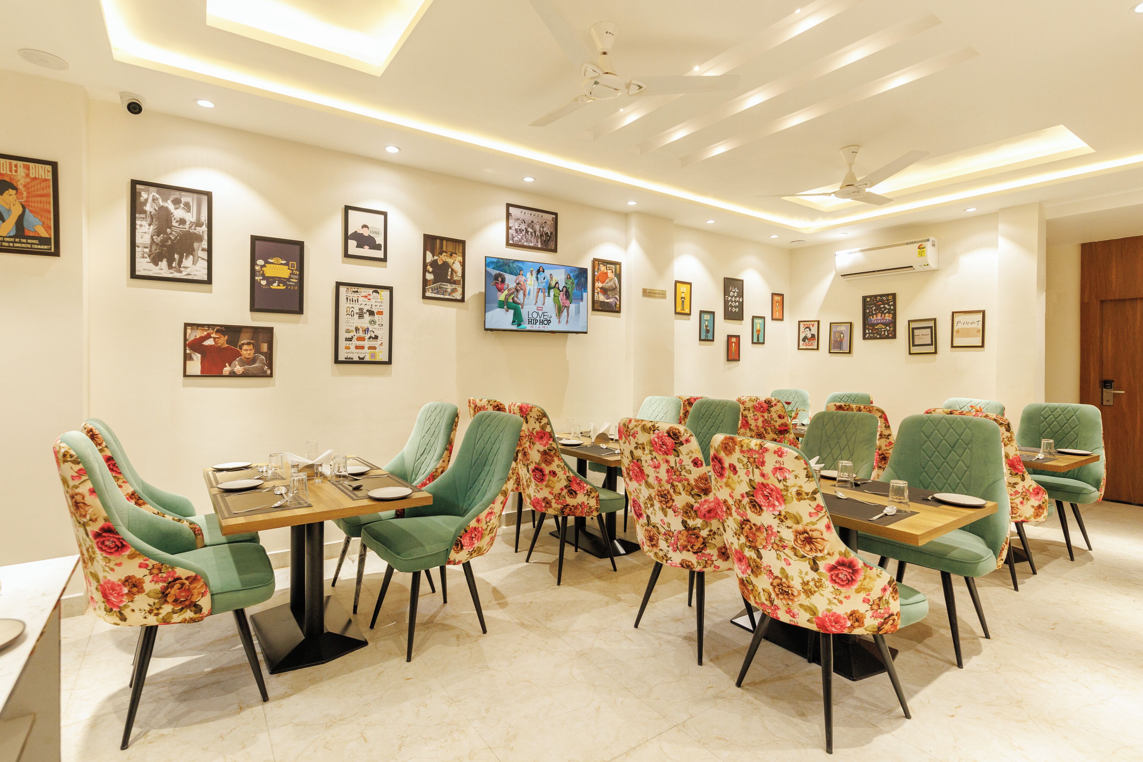 A dining area with green upholstered chairs, a wooden table, and framed pictures on the walls.