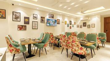 A dining area with green upholstered chairs, a wooden table, and framed pictures on the walls.