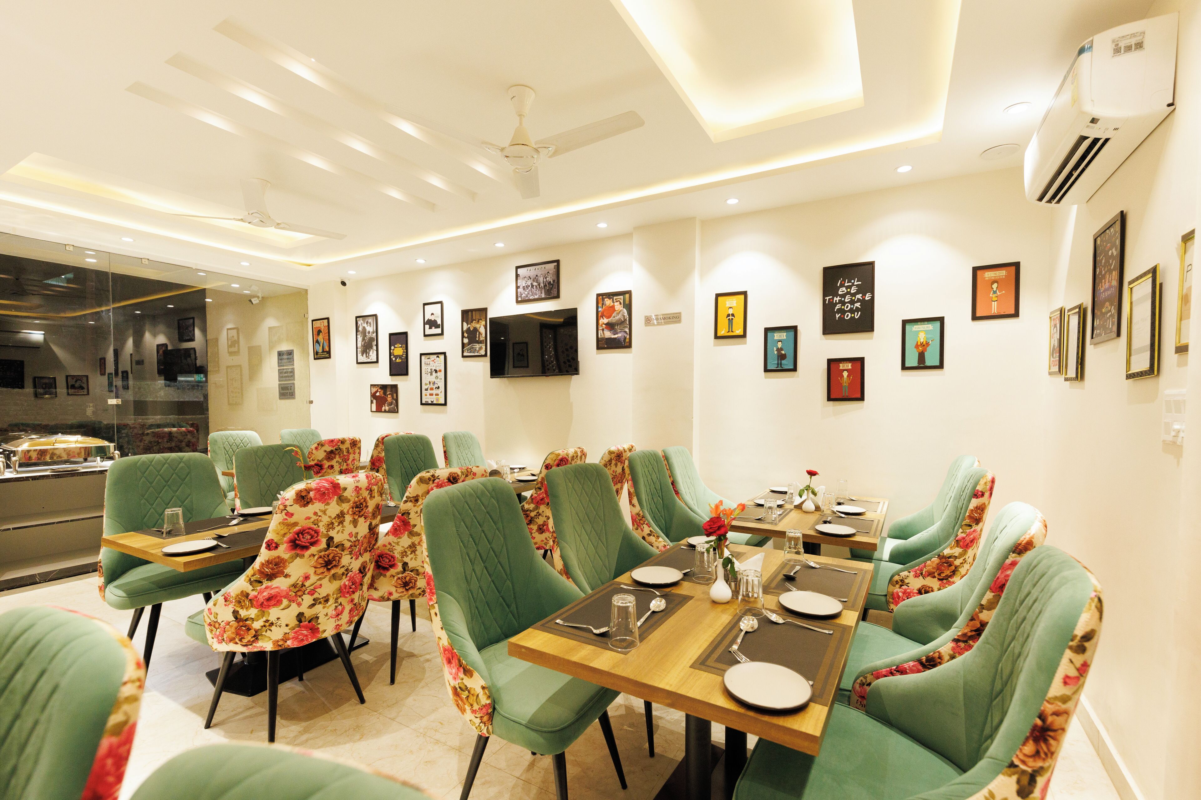 A dining area with green upholstered chairs, a wooden table set for four, and framed artwork on the walls.