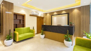 A modern reception area with a black marble counter, green sofas, and potted plants. - Veda Inn By Casa Ekam (Yamkeshwar)