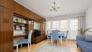 A living room with a wooden bookshelf, a TV, a dining table with chairs, a sofa, and a large window with curtains. - Spacious Apartment | 2 Bedrooms and Balcony close to the Center (Warszawa)
